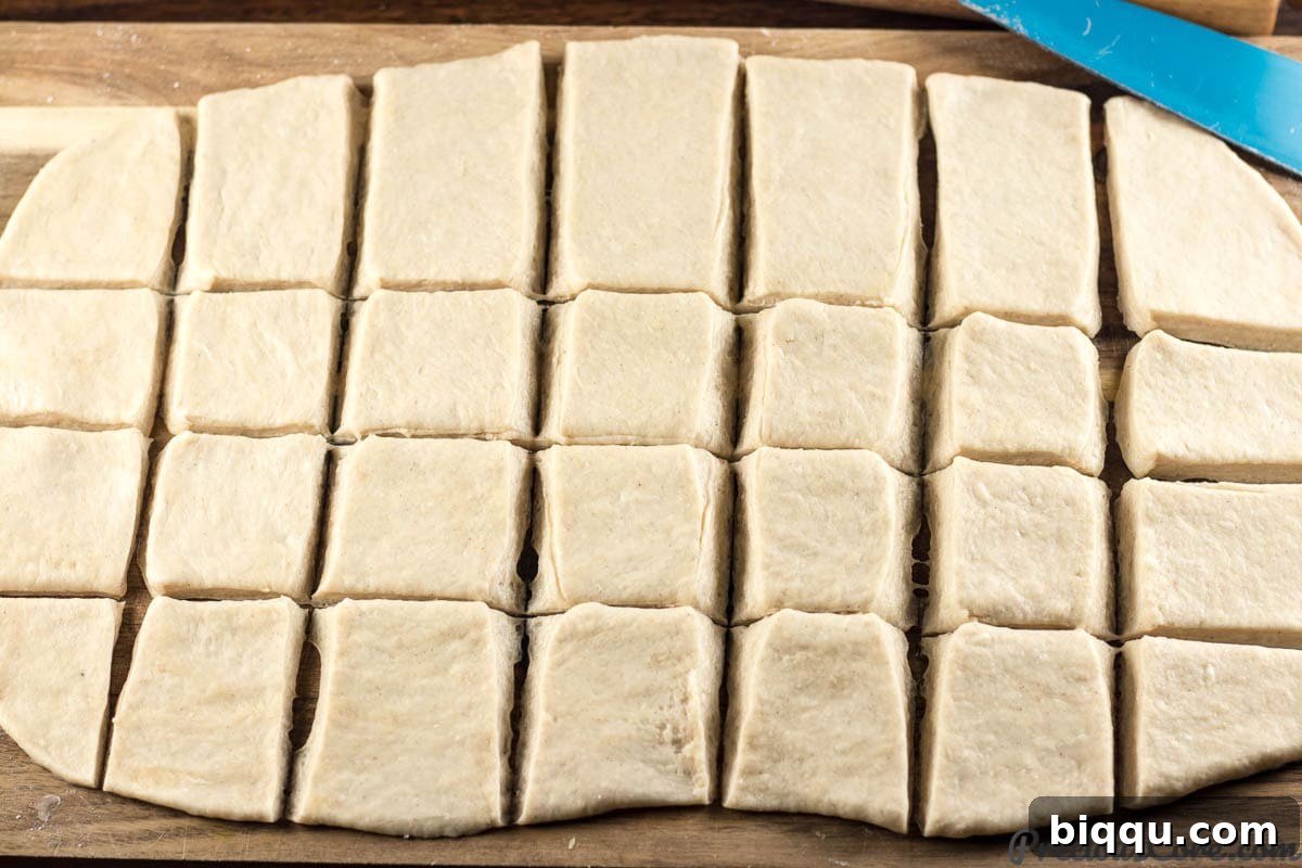 Mandazi East African Doughnuts 8 Mandazi dough rolled out and neatly cut into square pieces on a wooden board.