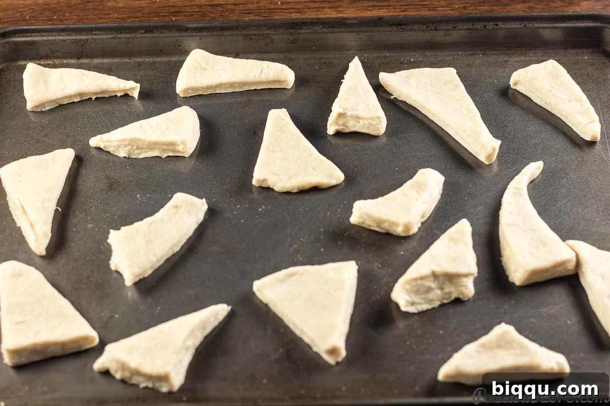 Mandazi East African Doughnuts 9 Numerous diamond-shaped Mandazi dough pieces arranged neatly on a wooden surface, ready for frying.