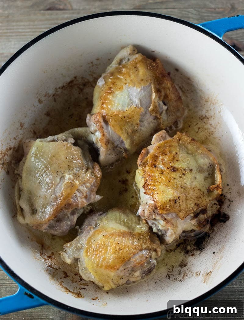 Crispy browned chicken thighs in a cast iron pot, ready for the next step in the stew.