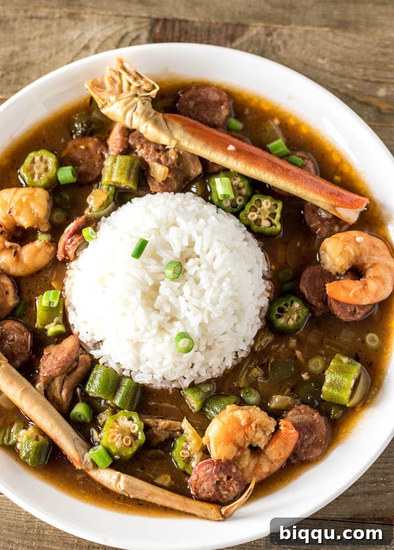 A bowl of steaming Seafood Gumbo served with fluffy white rice, featuring large shrimp, crab legs, and rich, dark broth.