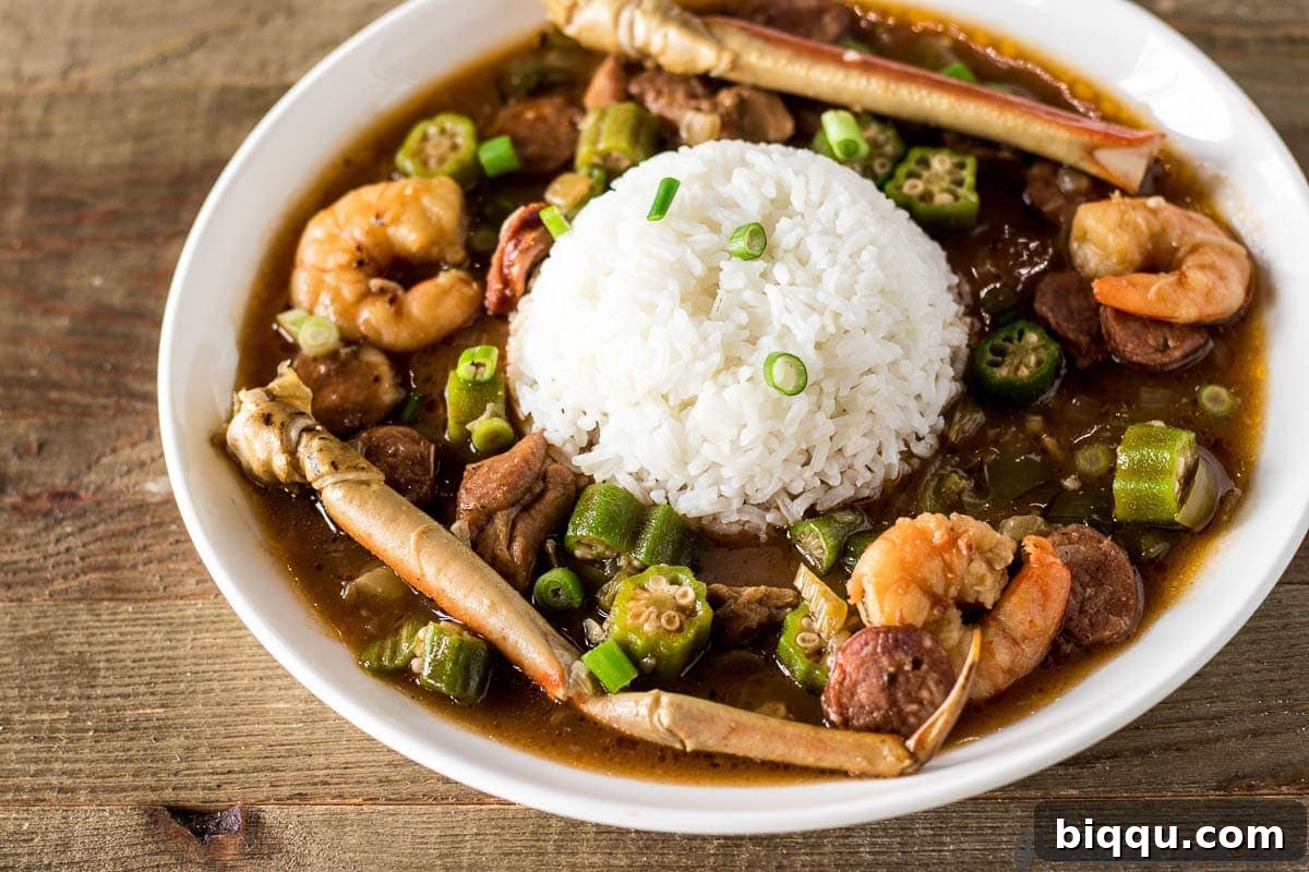 A large bowl of Seafood Gumbo featuring prominent shrimp and crab legs, served alongside white rice, ready to eat.