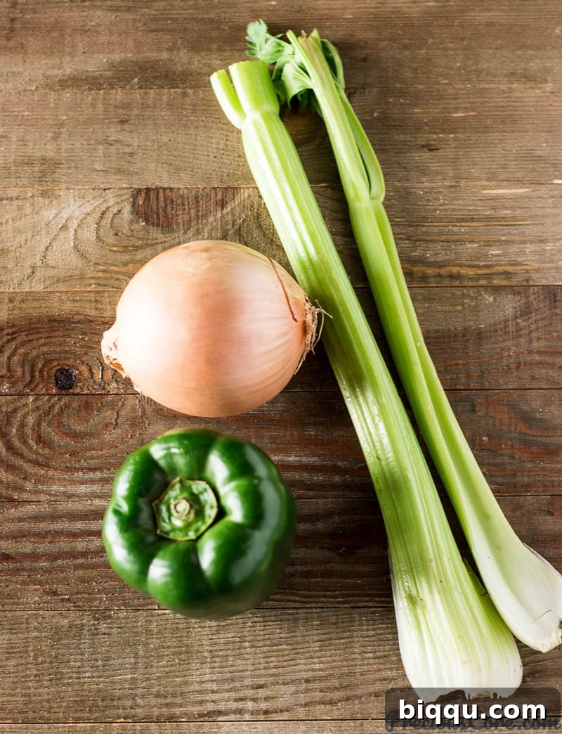 The holy trinity of cooking: diced onions, green bell pepper, and celery stalks on a cutting board.