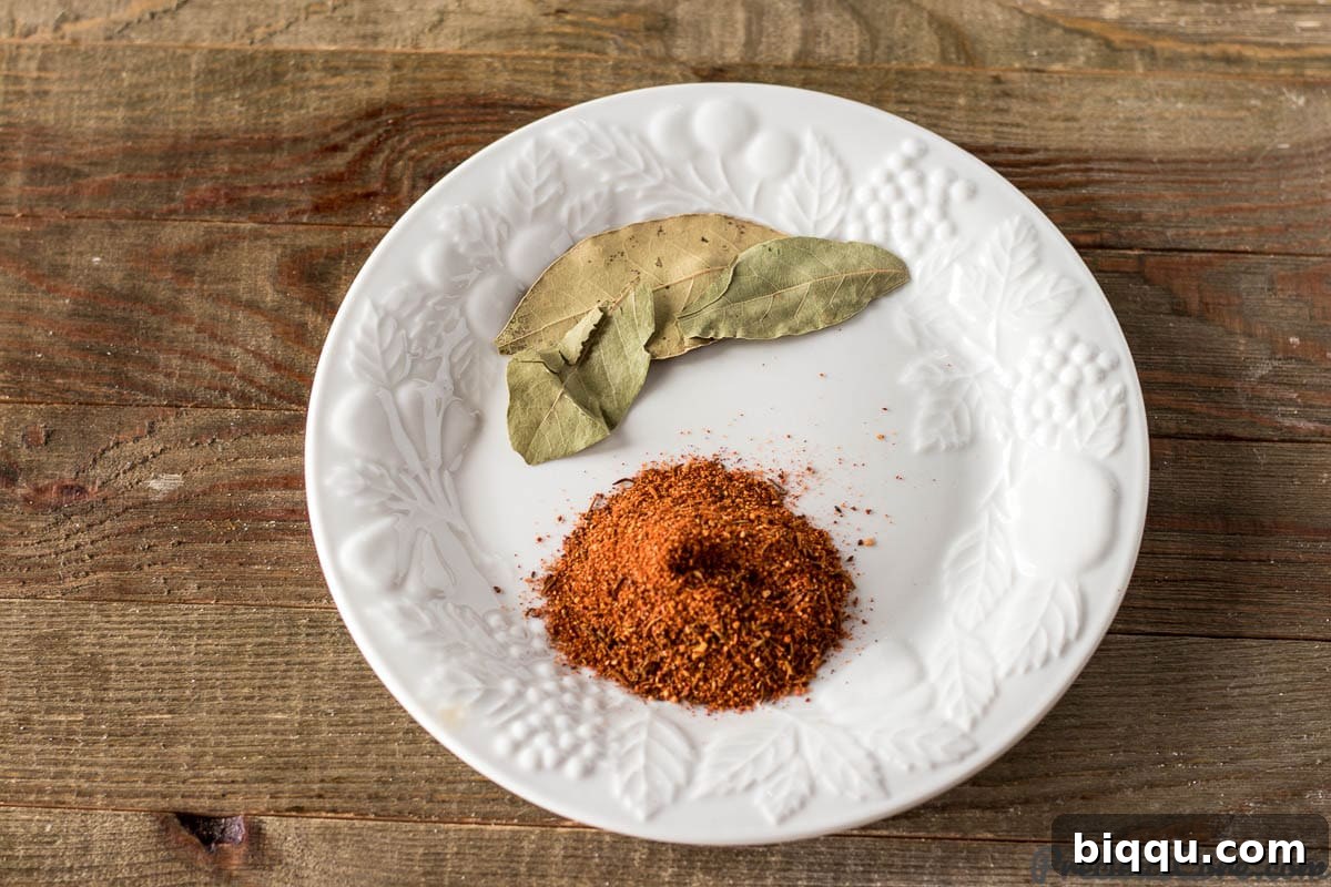 A small bowl of Creole seasoning with several bay leaves scattered around, ready to be added to a dish.