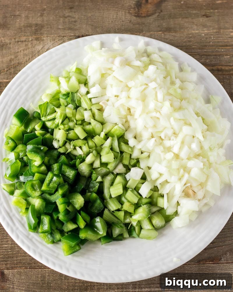 Diced onion, celery, and green bell pepper on a cutting board, prepared for the gumbo.