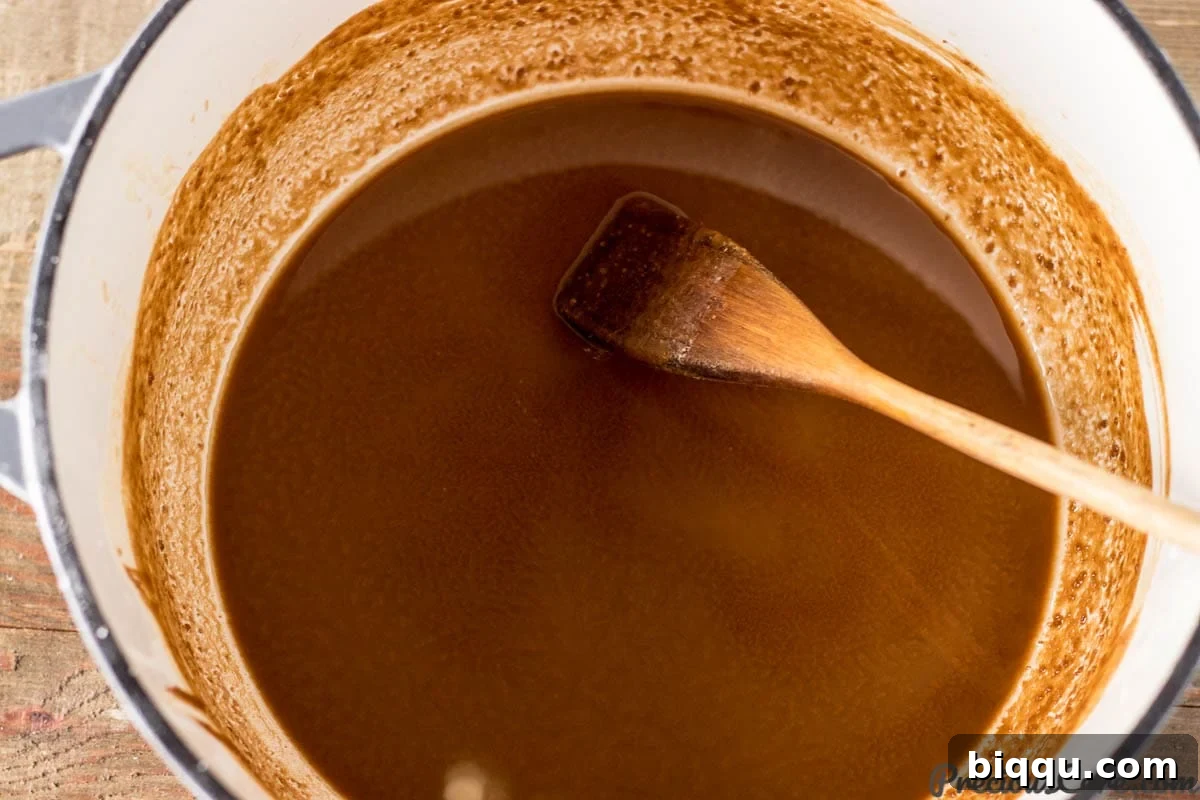 A wooden spoon stirring a dark chocolate-colored roux in a cast iron pot, illustrating the crucial step in gumbo making.