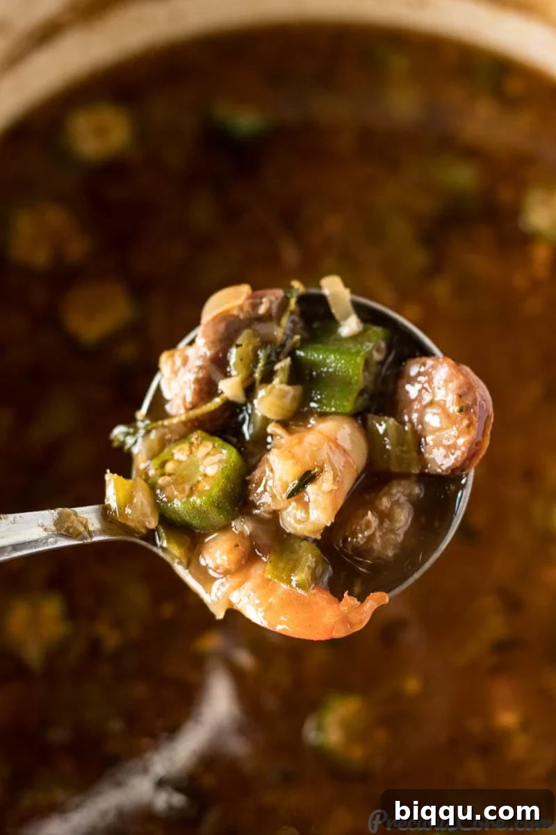 Rich seafood gumbo simmering in a pot, with visible okra, shrimp, and sausage chunks.