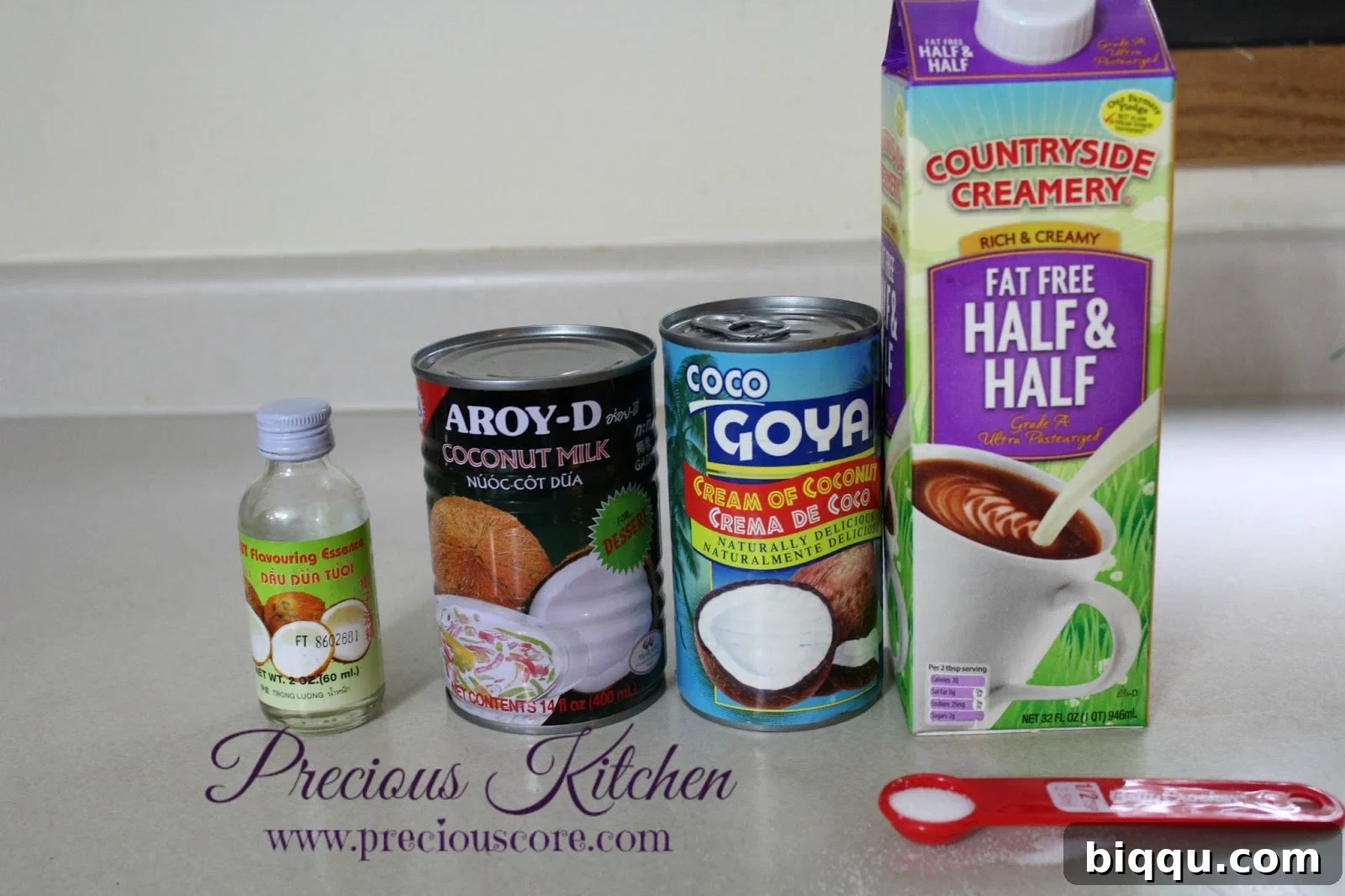 A selection of ingredients laid out, including cans of coconut milk and cream of coconut, and a measuring cup with heavy cream.