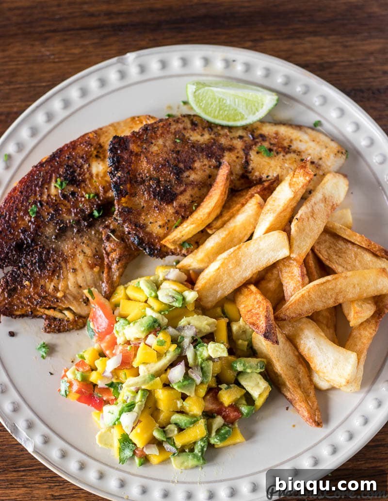 Grilled fish served with a vibrant wedge of lime and a generous scoop of Mango Avocado Salsa on the side.
