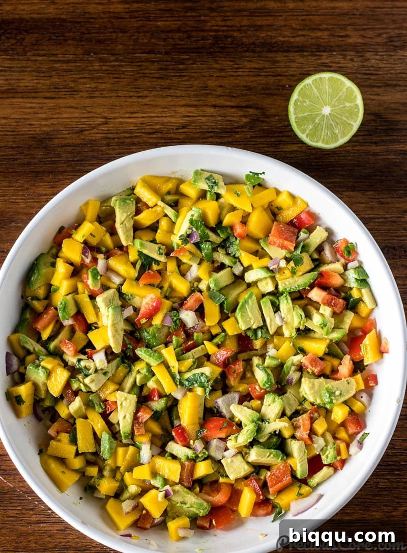 A vibrant Mango Avocado Salsa presented in a large white serving bowl, with a half-lime wedge placed invitingly on the side.