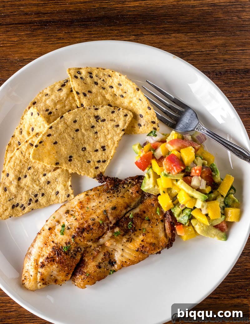 A beautifully plated dish featuring grilled fish, a lime wedge, and a generous portion of Mango Avocado Salsa, alongside a side of tortilla chips.