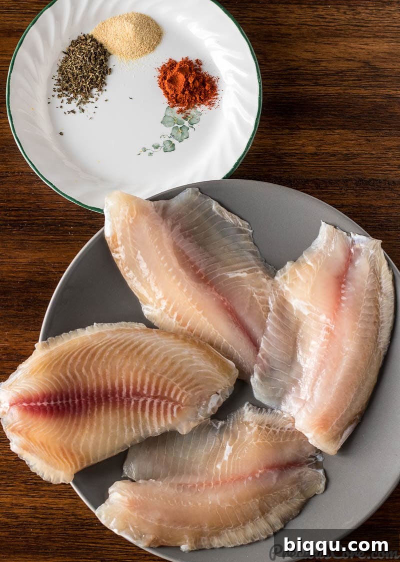 Fresh tilapia fillets on a plate alongside small dishes of dried spices for seasoning.