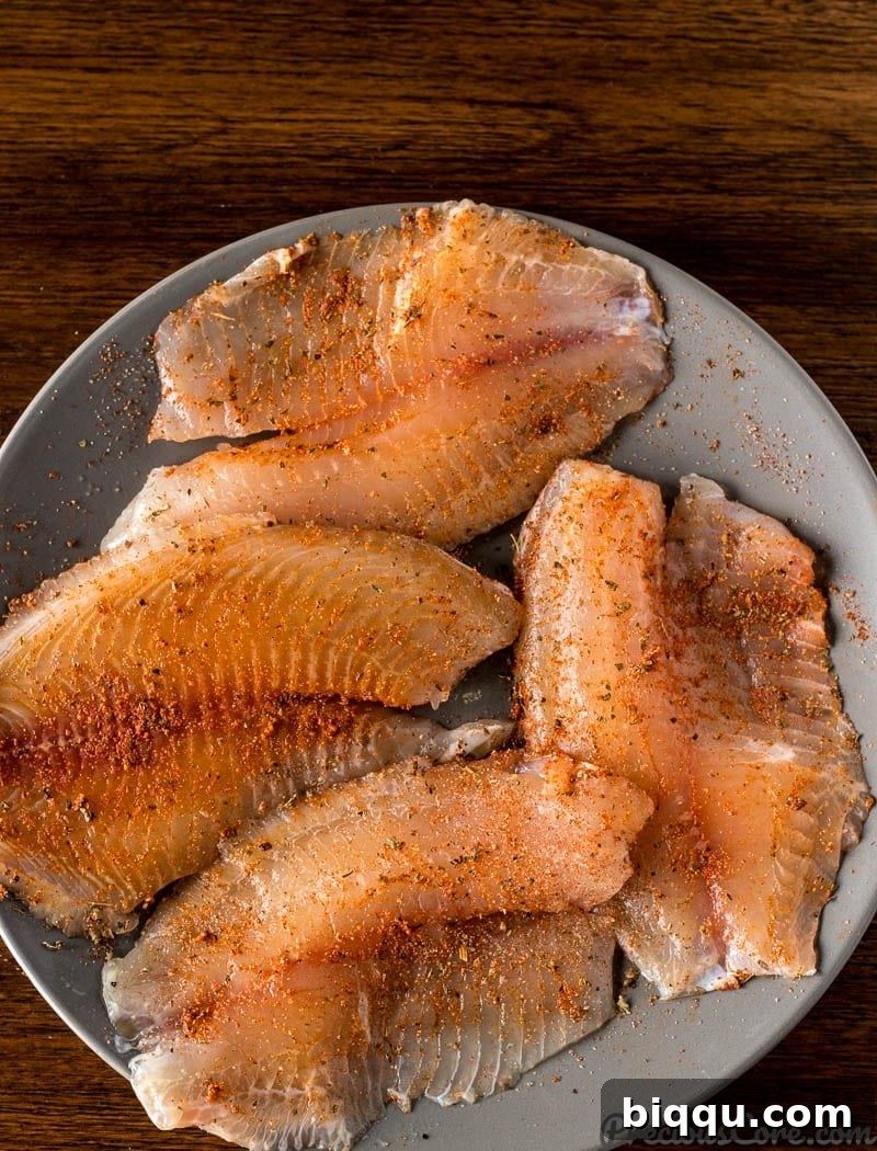 Tilapia fillets expertly seasoned with a blend of spices, ready for searing.