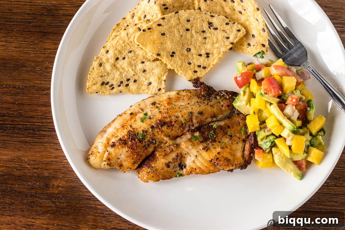 Pan Seared Tilapia served on a plate alongside fresh Mango Avocado Salsa and crunchy tortilla chips.