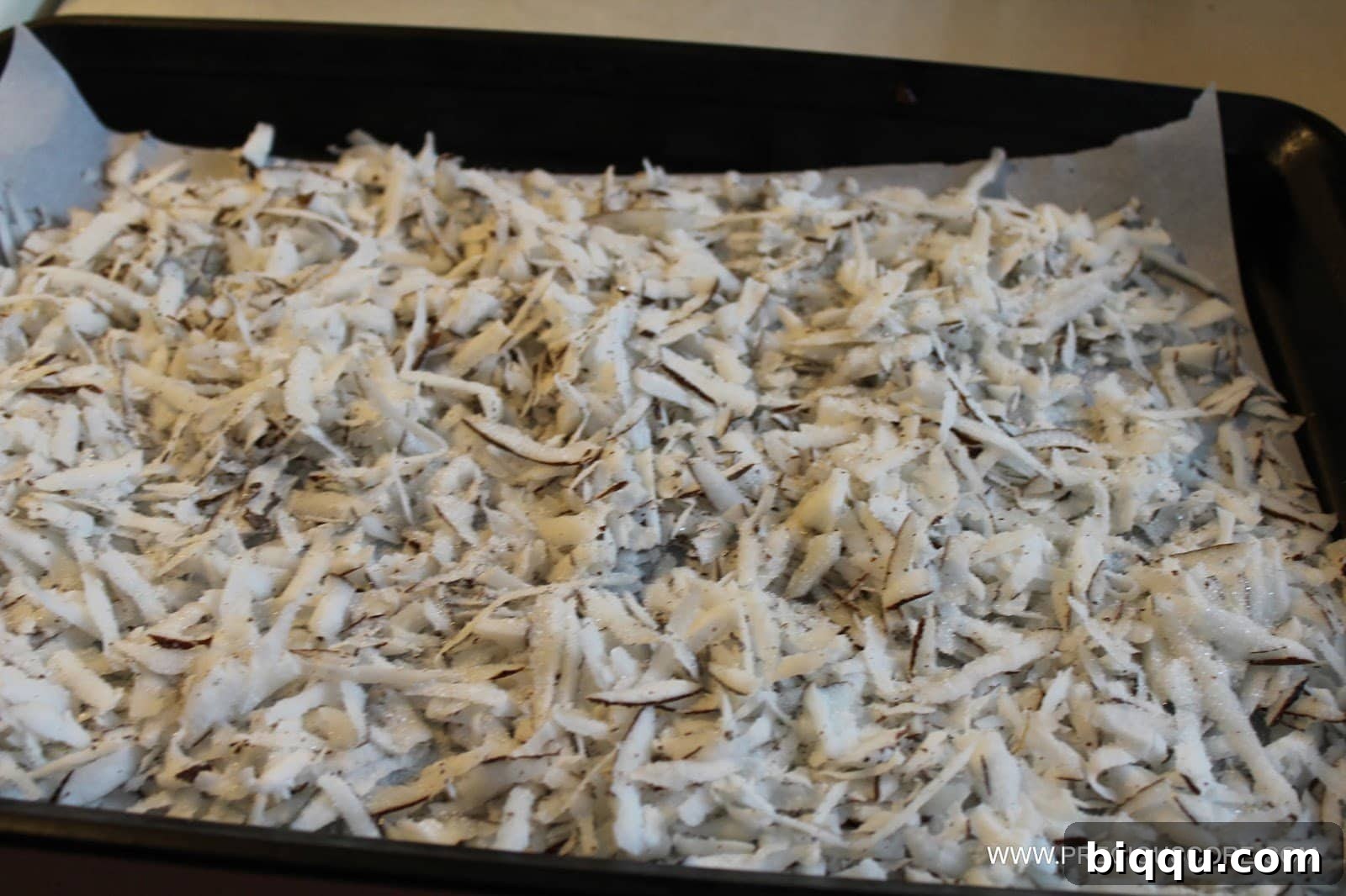 Shredded coconut sprinkled with sugar on a baking sheet, ready for the oven.