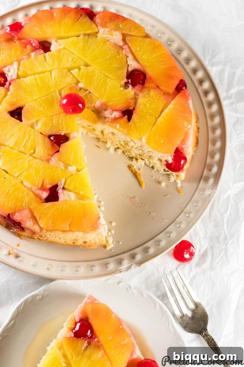 A delectable slice of homemade Pineapple Upside Down Cake, revealing its golden pineapple topping and a vibrant maraschino cherry in the center.