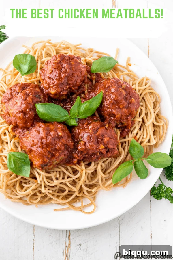 A close-up picture of delicious chicken meatballs resting on a bed of perfectly cooked spaghetti, coated in a rich, vibrant tomato sauce.