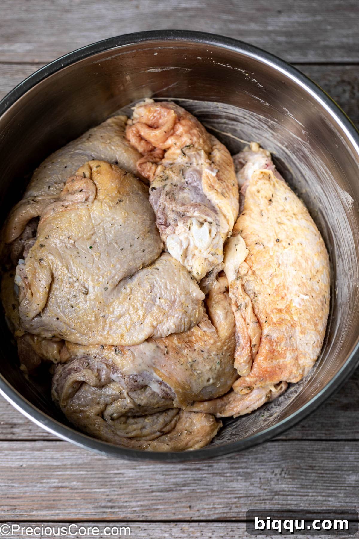 Seasoned chicken thighs coated in a rich mayonnaise marinade, resting in a stainless steel mixing bowl.