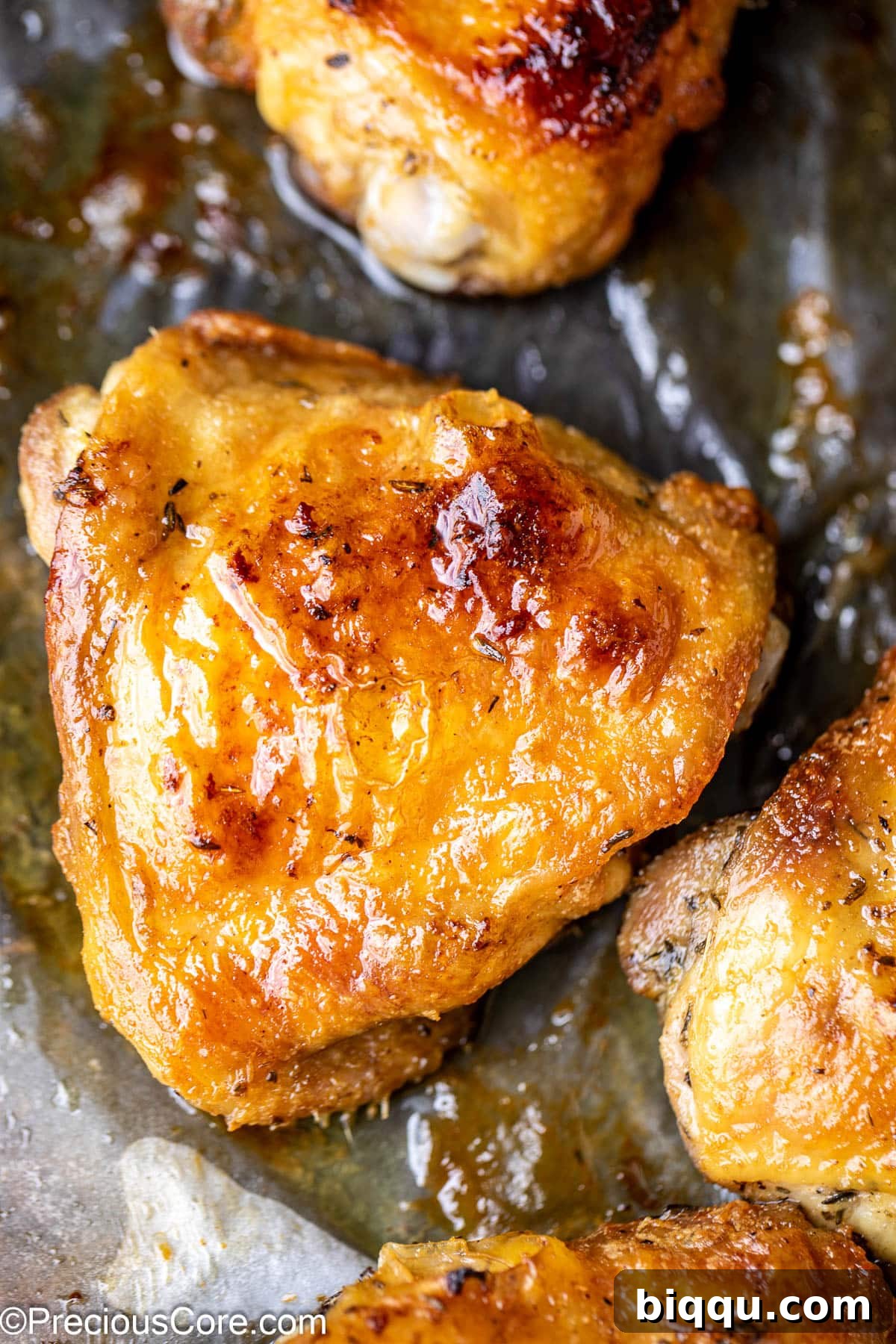 Close up on a glistening golden brown chicken thigh on parchment paper, fresh out of the oven.