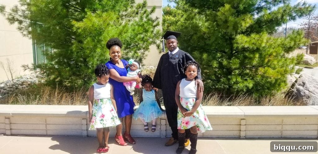 A graduate proudly stands in his cap and gown, surrounded by his loving wife and four children, a testament to family support.