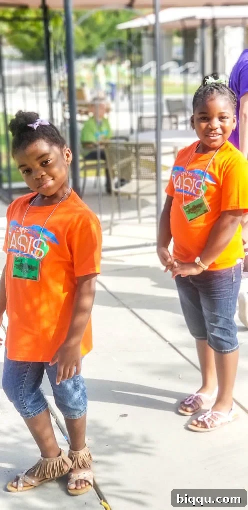 Two joyful girls in vibrant orange t-shirts, smiling brightly after a fun summer camp experience.