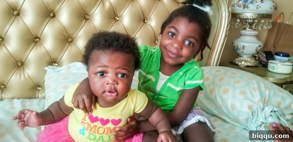 A sweet girl, Yoyo, smiling with her arms lovingly wrapped around a baby, showcasing her role as an amazing big sister.