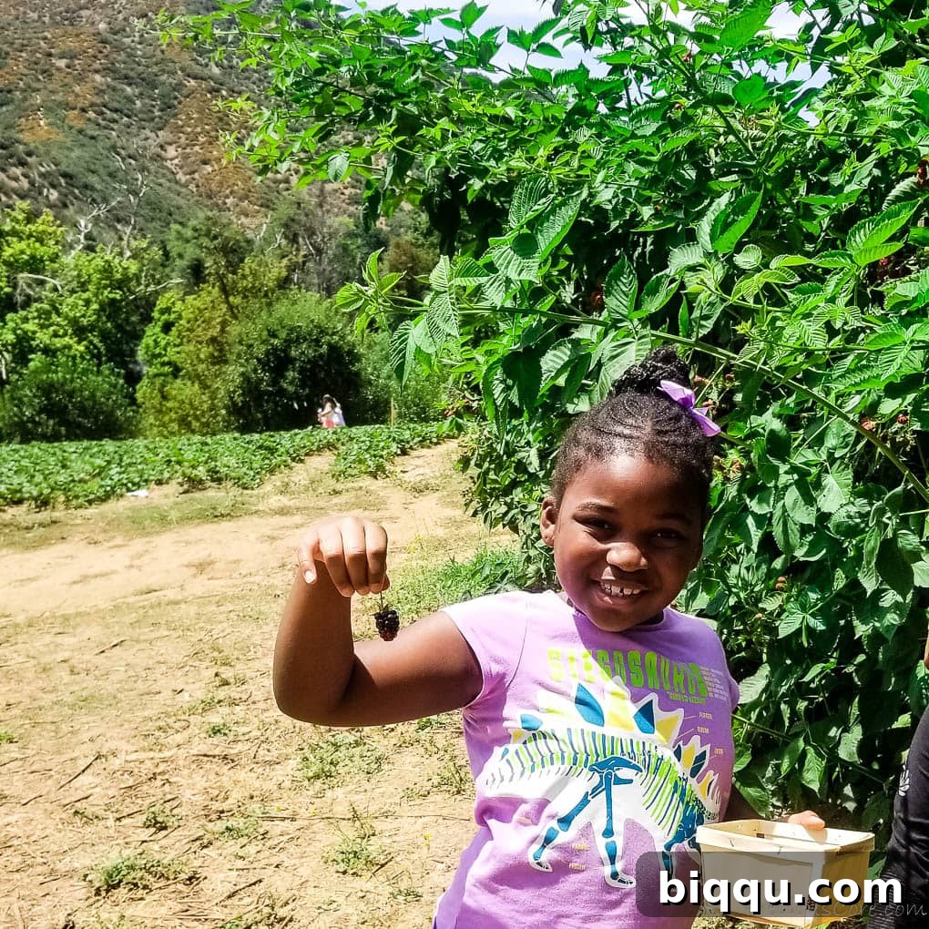 A happy girl smiling widely, proudly holding a freshly picked berry, radiating the joy of summer.
