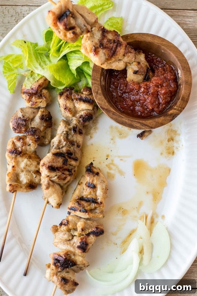 Gourmet chicken skewers served with a side of hot sauce and fresh vegetables