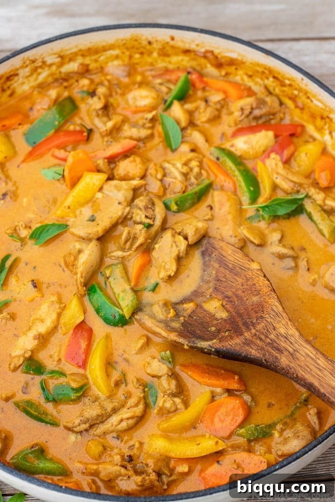 Coconut curry chicken simmering in a large pot on the stove, showing rich texture and vibrant colors.