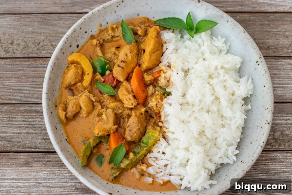 A close-up of a bowl of creamy coconut curry chicken served alongside a generous portion of white rice.