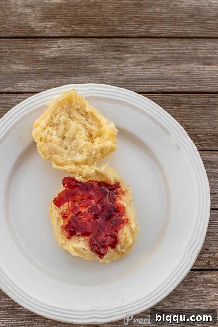 A single homemade biscuit on a plate with jam spread on top, ready to eat.