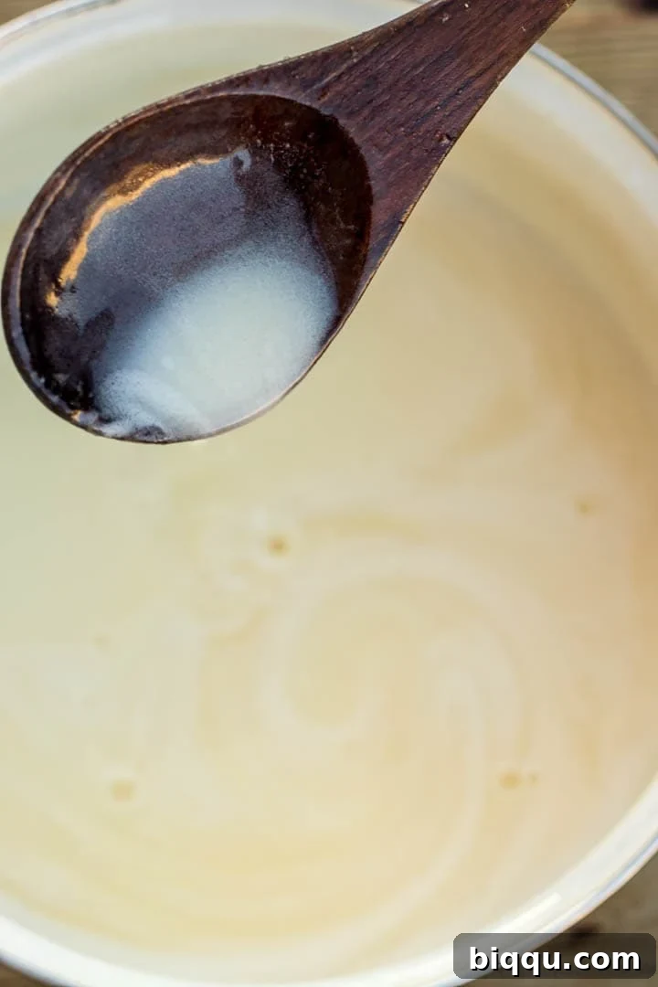 A spoon pouring warm bread pudding sauce into a bowl, demonstrating its smooth, flowing, and pourable texture while still hot.