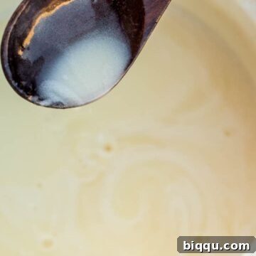 A spoonful of creamy Bread Pudding Sauce being poured, illustrating its rich texture and readiness for serving.