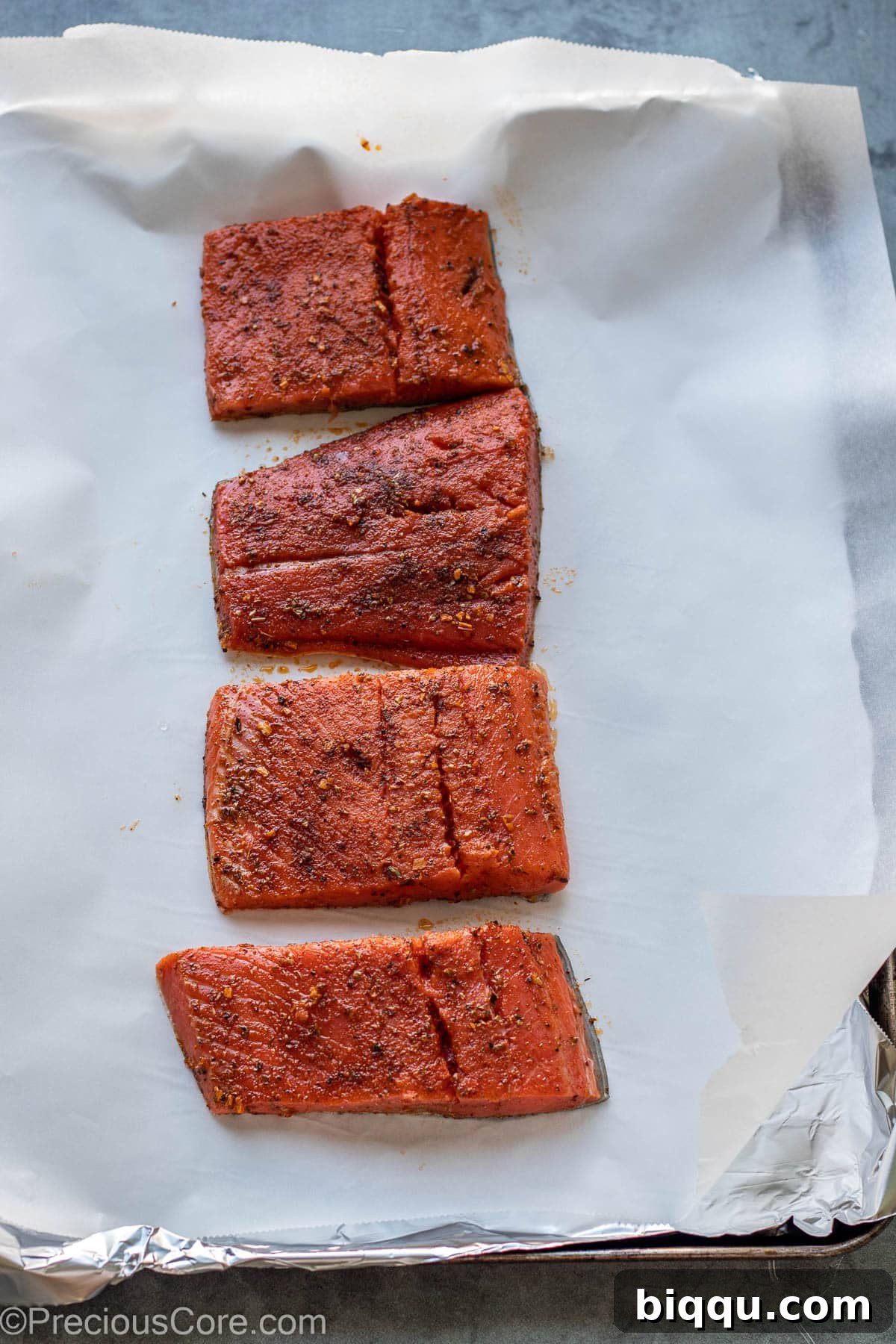 Seasoned cajun salmon fillets placed on a baking sheet lined with parchment paper, ready for baking.