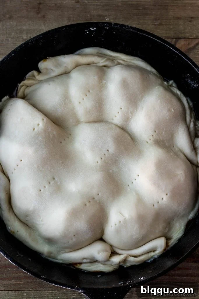 Puff pastry carefully placed over the apples, with edges neatly tucked into the skillet