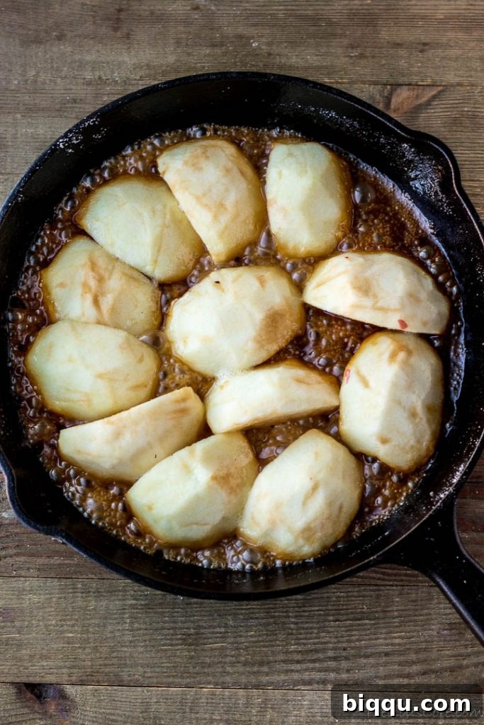 Close-up view of apples simmering in a rich caramel sauce in a cast-iron skillet