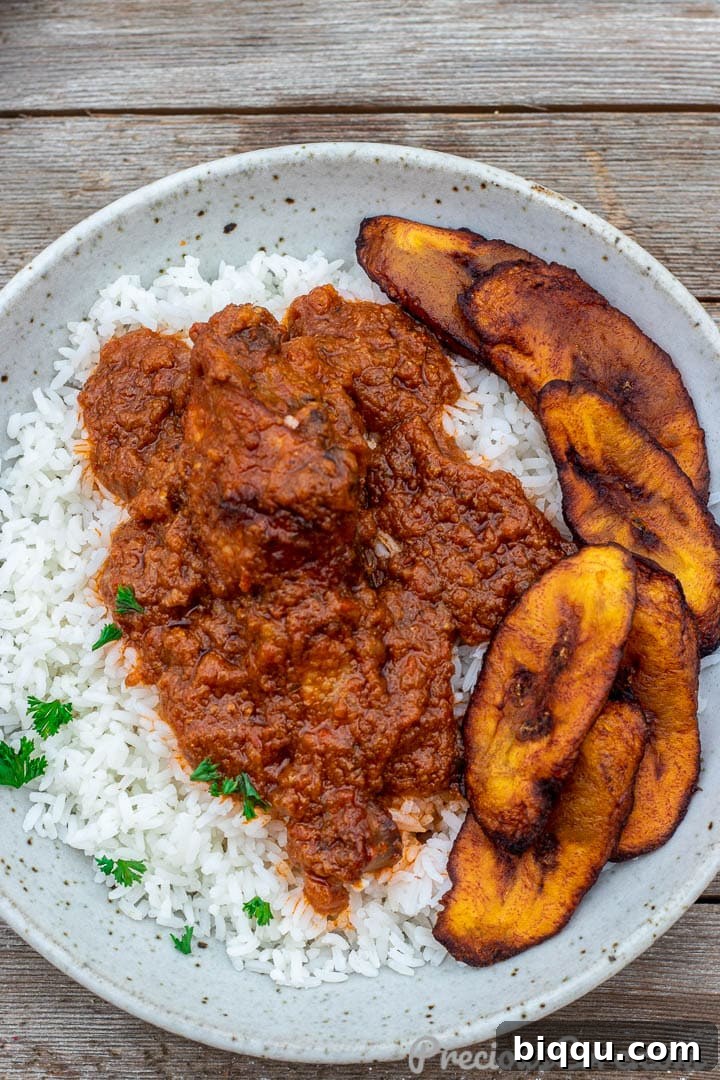 Bowl of African chicken stew served over rice with a side of plantains.