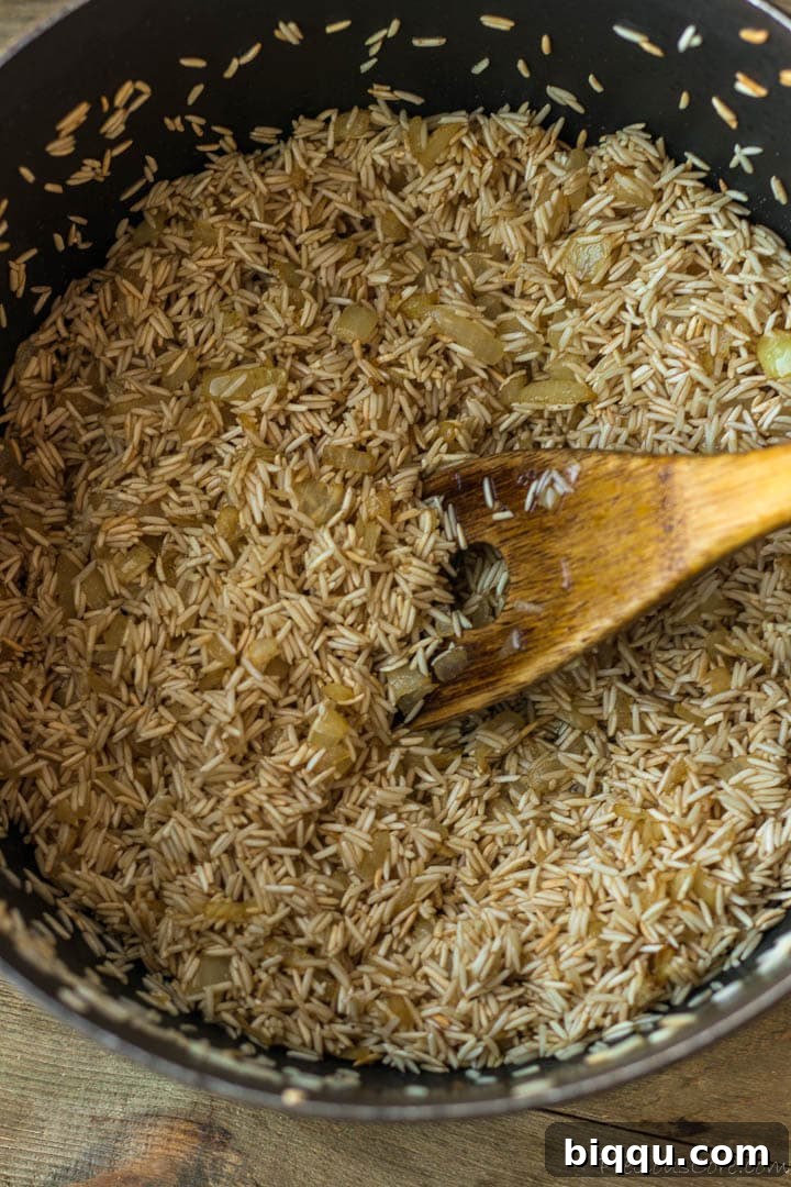 Raw basmati rice being toasted with sautéed onions and oil in a pot, developing nutty flavors.